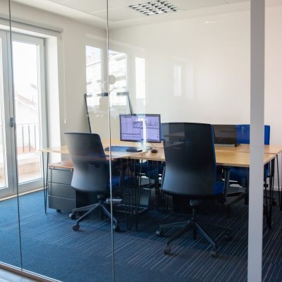Empty boardroom behind glass wall Empty boardroom behind glass wall. Meeting room with conference table, shared desk for team and workplaces. Trading graphs on monitor. Office interior or commercial real estate concept